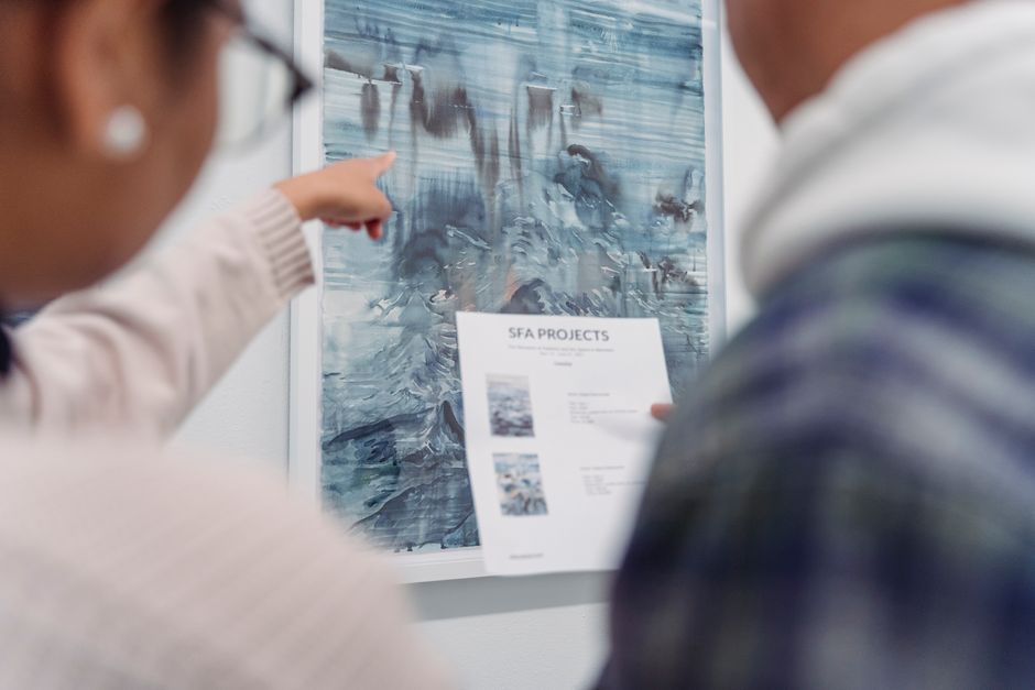Two adults discuss an abstract painting, pointing and holding a document.
